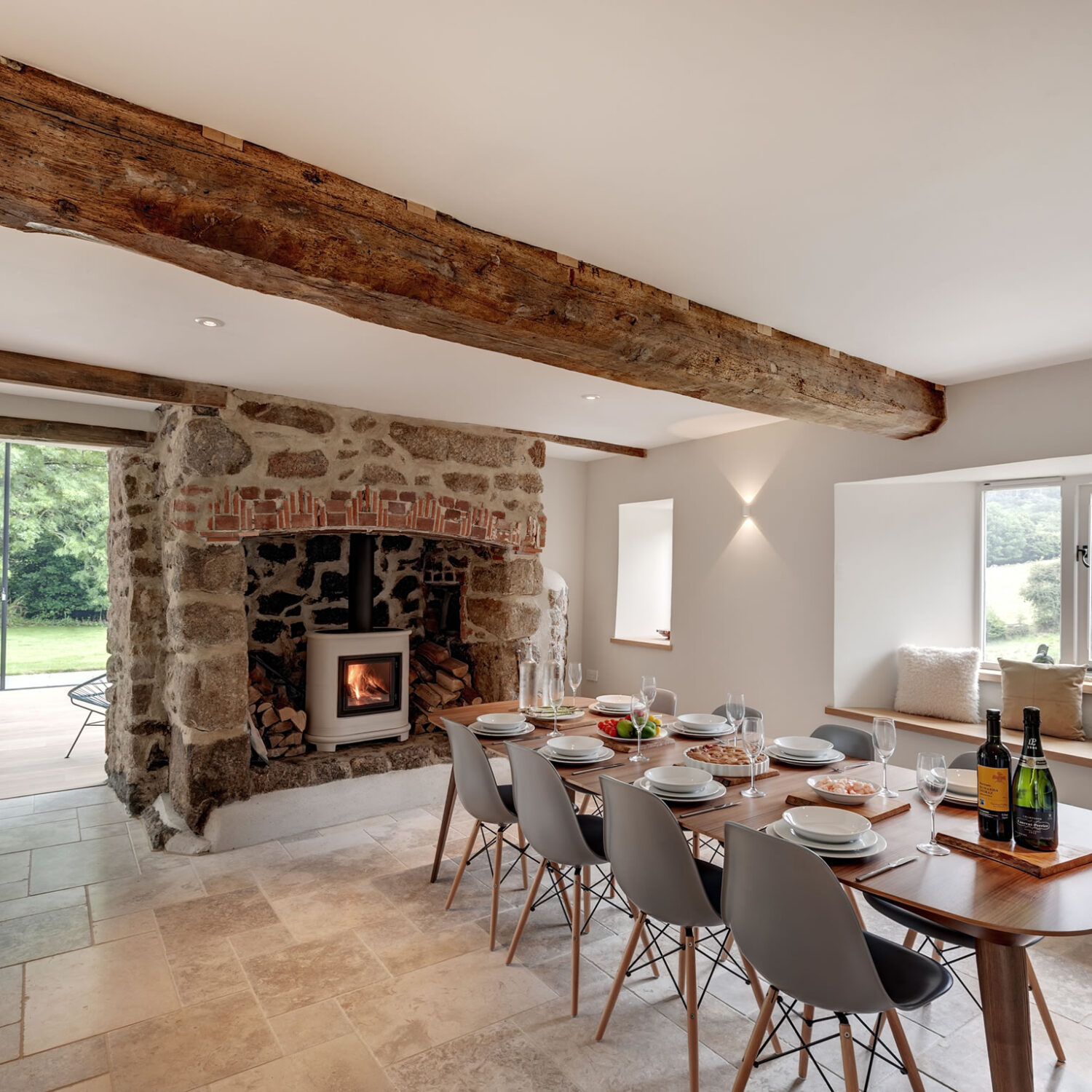 Modern farmhouse dining room with original oak timber beams, limestone flag floor and granite fireplace. Contemporary mid-century furniture acts as a counterpoint.