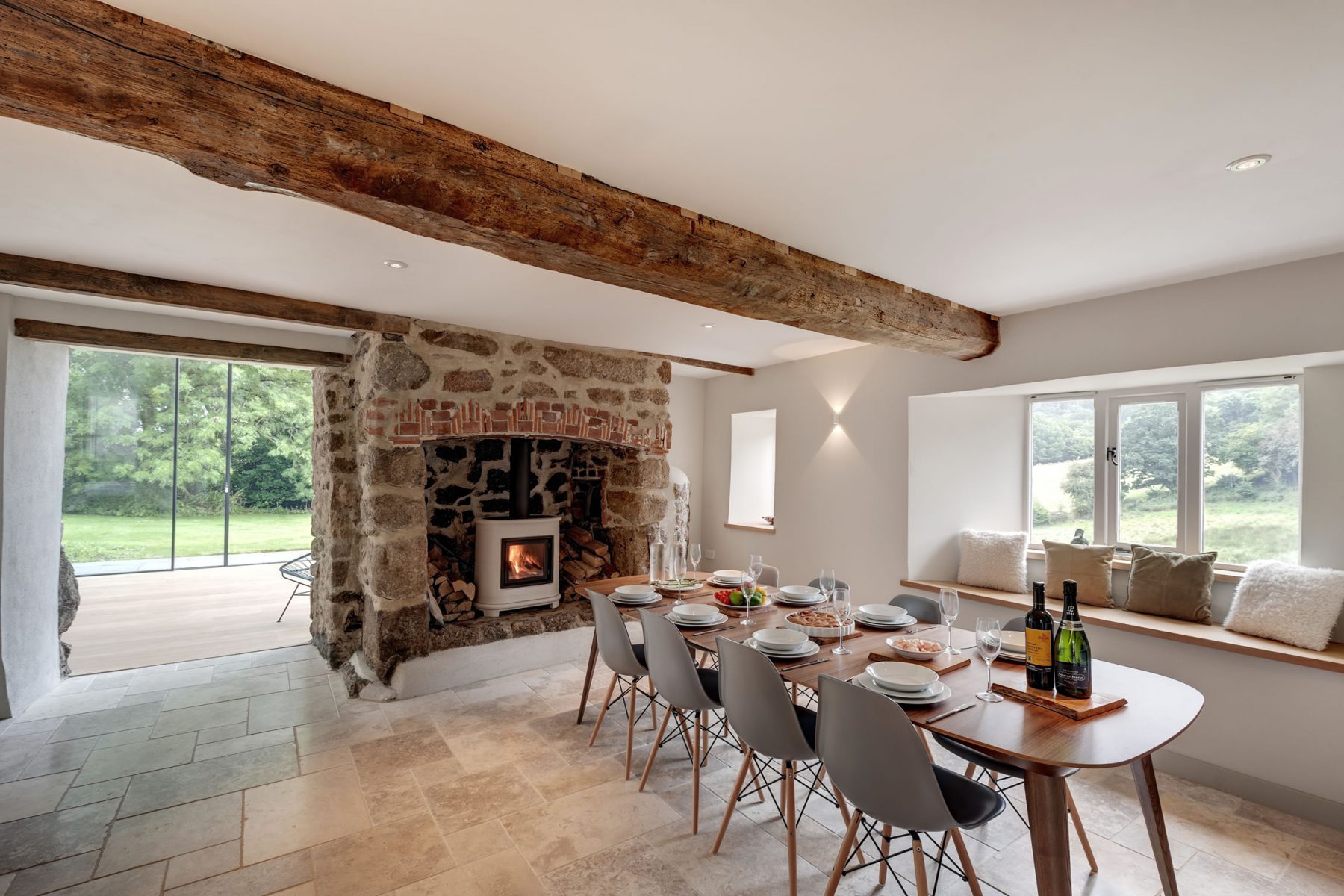 Modern farmhouse dining room with original oak timber beams, limestone flag floor and granite fireplace. Contemporary mid-century furniture acts as a counterpoint.