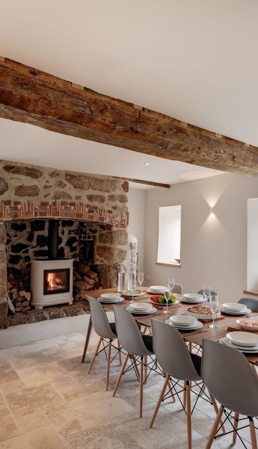 Modern farmhouse dining room with original oak timber beams, limestone flag floor and granite fireplace. Contemporary mid-century furniture acts as a counterpoint.