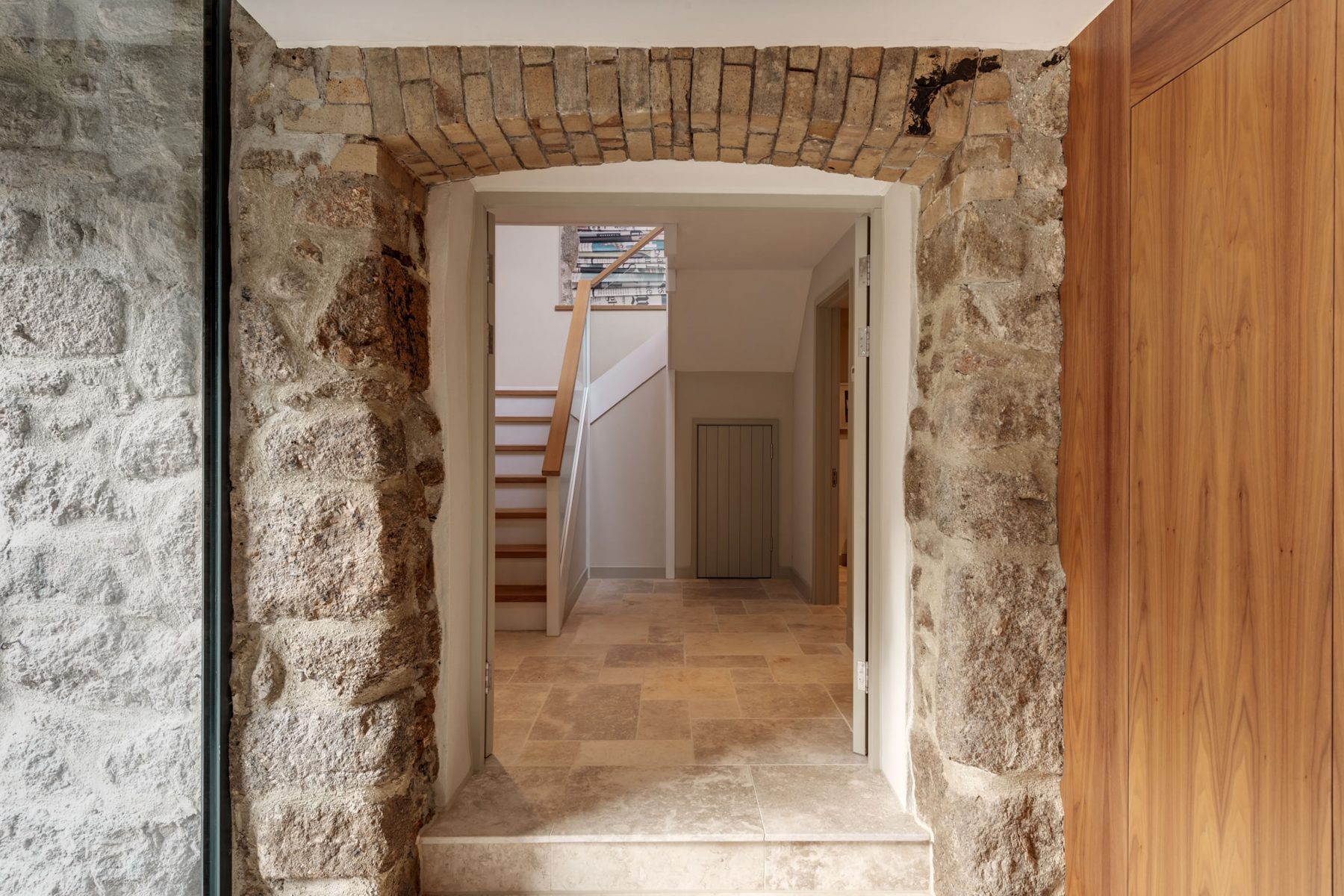 Original stone arch doorway with limestone steps, American black walnut joinery cupboards, and frameless glass window.