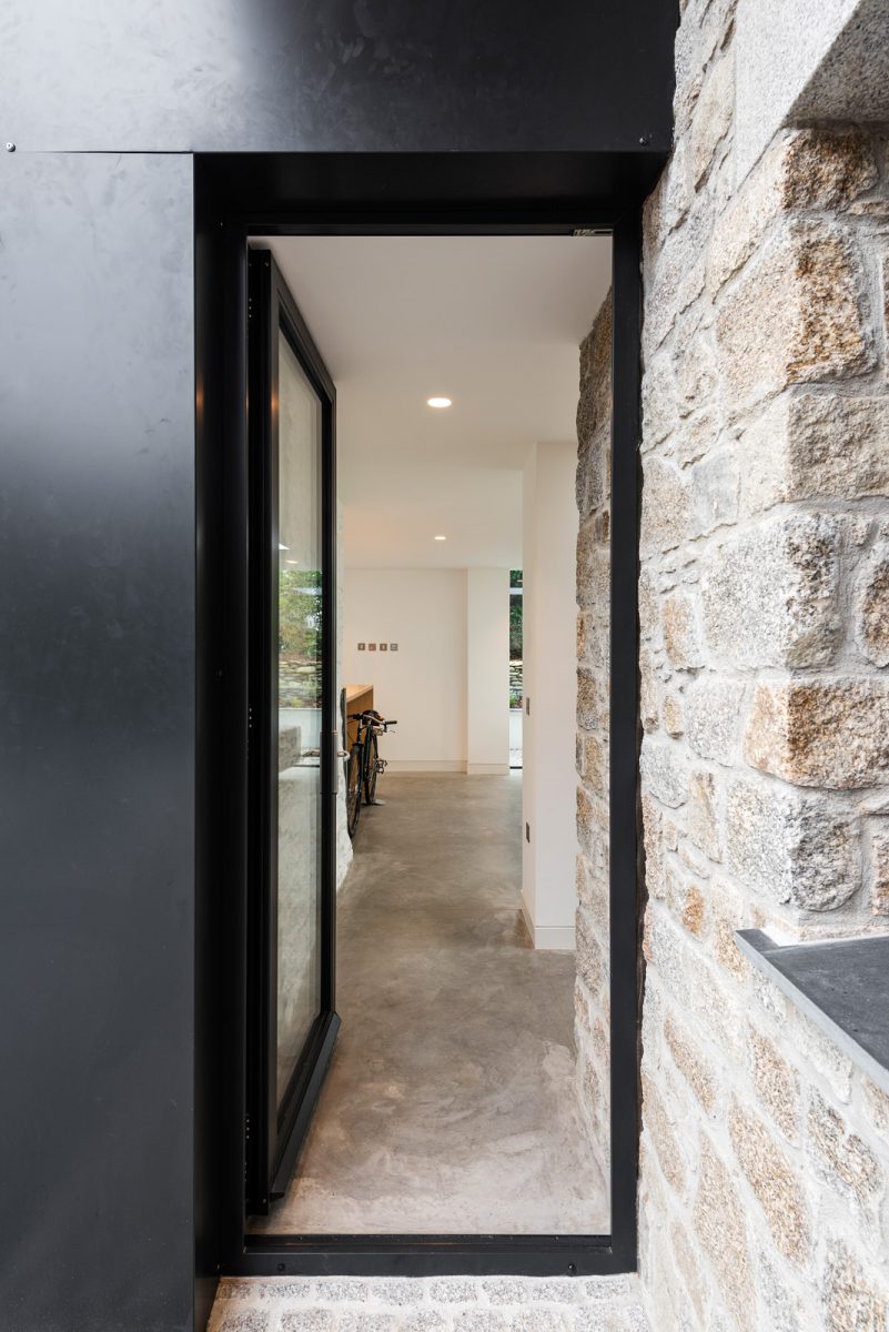 Granite wall of barn with glazed aluminium front door and aluminium wrapped feature panel surround.