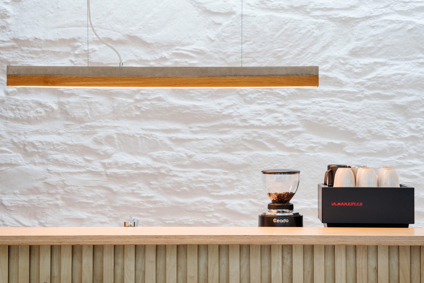 Concrete and timber light over coffee island joinery. White painted stone wall of Cornish cottage behind.