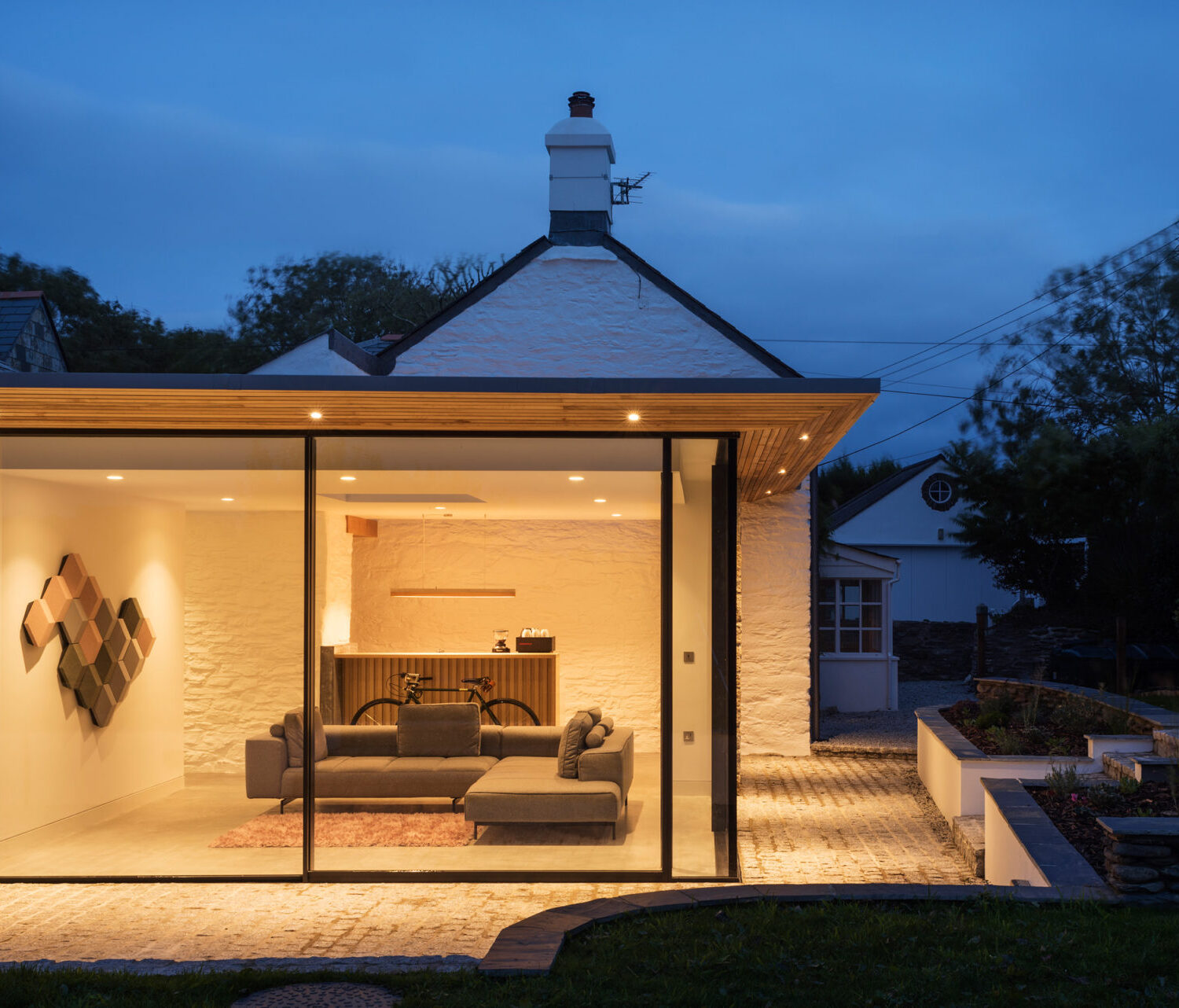 Highly glazed extension to a traditional Cornish cottage, with sliding glass doors and elegant roof overhang.