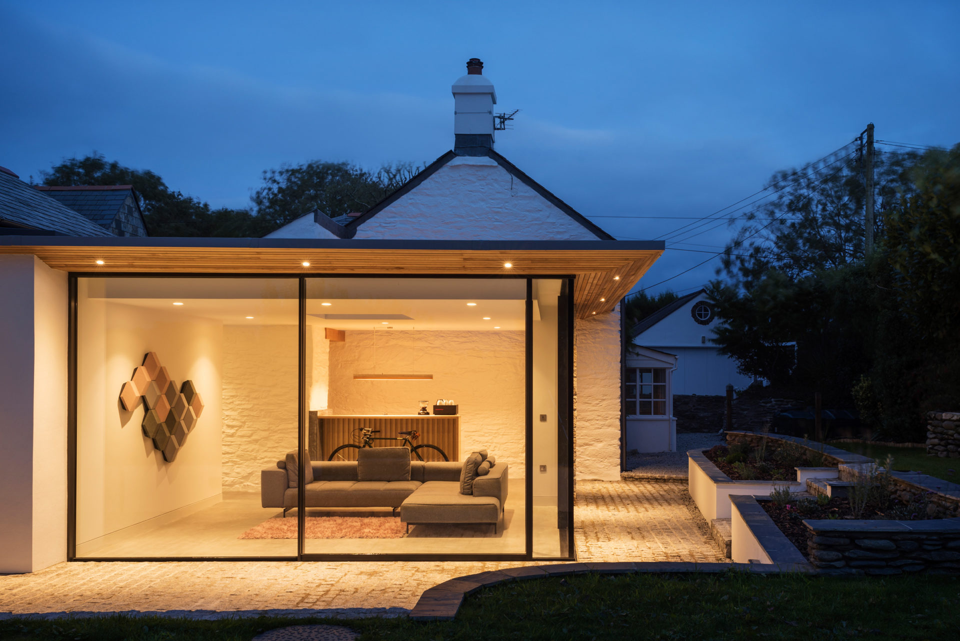 Highly glazed extension to a traditional Cornish cottage, with sliding glass doors and elegant roof overhang.